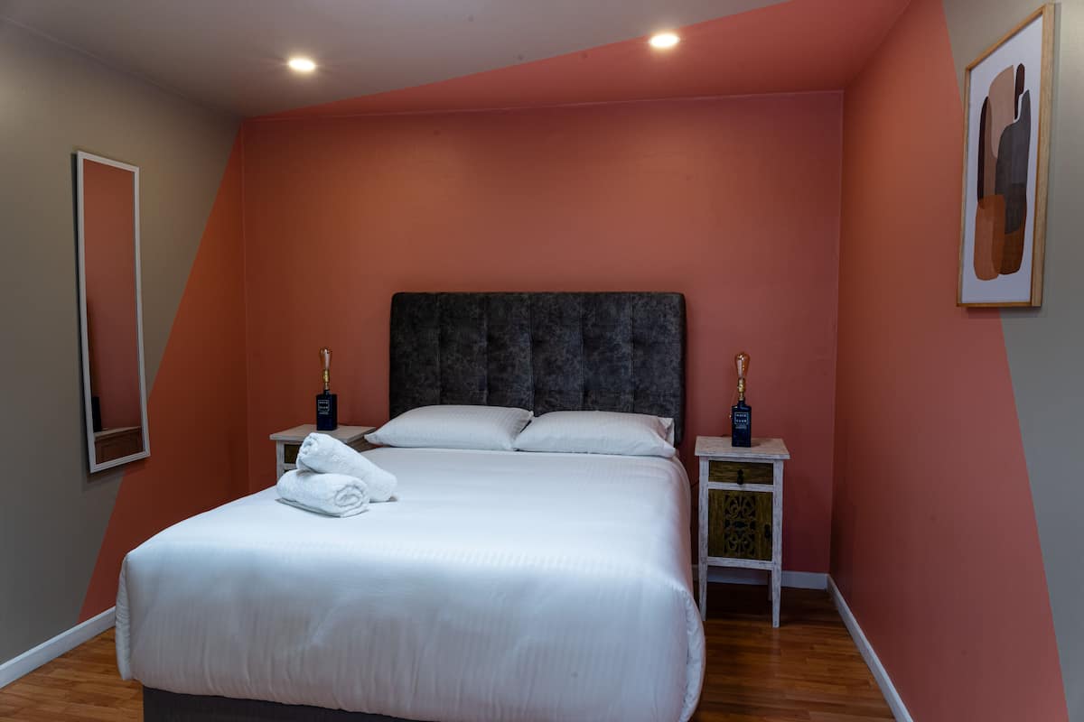 A neatly made bed with white linens and pillows, a dark headboard, and two bedside tables with decorative vases.