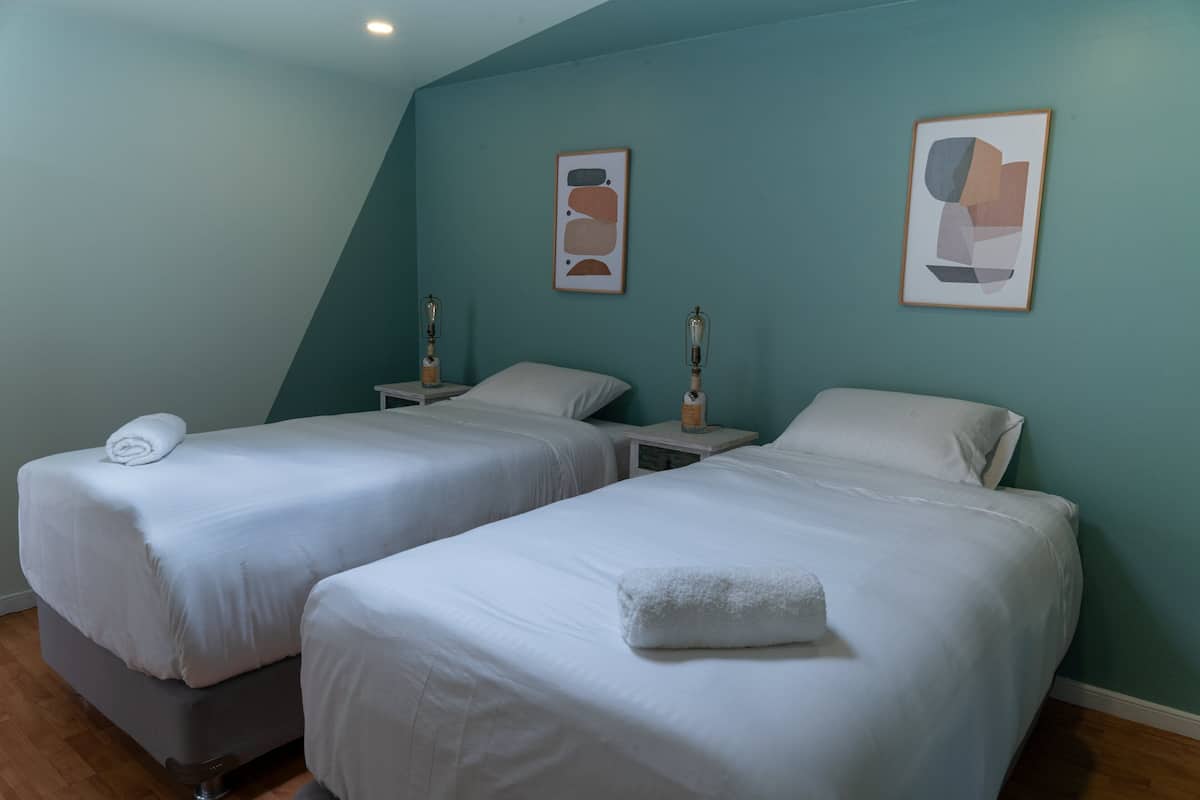 A room with two single beds, each with a white bedspread and pillows, and a small bedside table with a lamp.