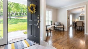 Ein modernes Interieur mit einer dunklen Haustür, einem Essbereich mit einem kleinen Tisch und Stühlen, und einer durchgehenden Tür erkennbaren Küche.