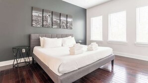 A modern bedroom with a large bed, grey walls, and a cityscape artwork. - The Taylor (Nashville)