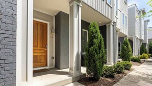 A modern townhouse with a wooden front door, a brick wall, and a well-maintained front yard with shrubs. - The Taylor (Nashville)