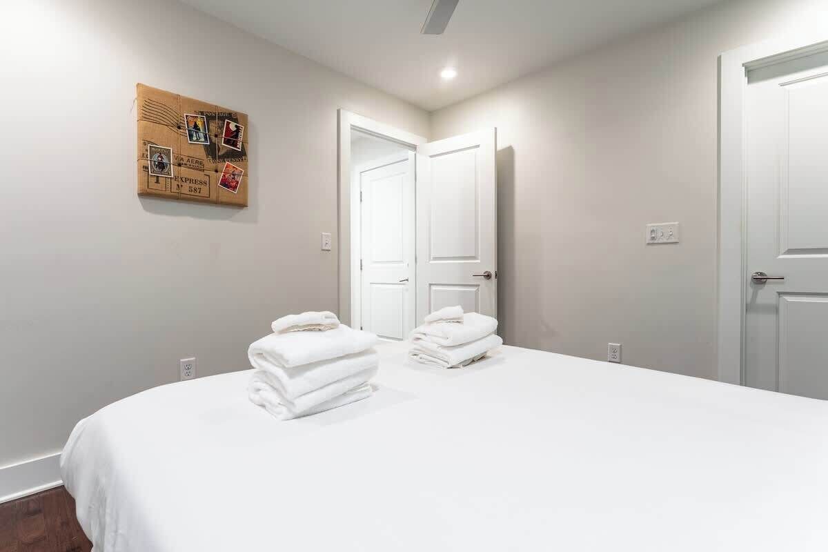 A bedroom with a bed, two stacks of white towels, a bulletin board with postcards, and two white doors.