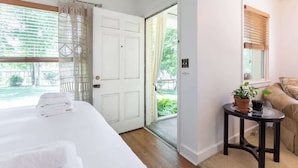 Ein Hotelzimmer mit einem Bett, einem kleinen Tisch mit Pflanze, einer Couch und einer Tür, die auf einen Balkon führt.