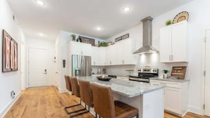 A modern kitchen with white cabinets, a stainless steel range hood, a marble island with bar stools, and a welcome sign.