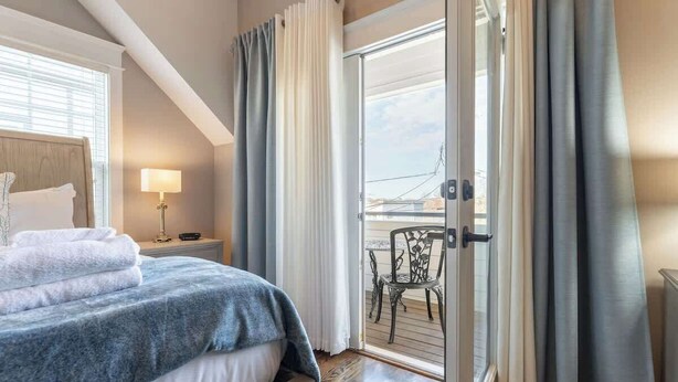 Habitación de hotel con cama, mesita de noche, lámpara y vistas al balcón.