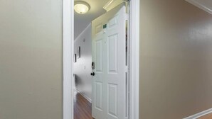 Un couloir avec une porte blanche portant le numéro 7, un plancher en bois et un luminaire au plafond.