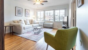 Un salon moderne avec un canapé blanc, un fauteuil vert, une table basse et un ventilateur de plafond.