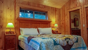 A wooden-paneled bedroom with a large bed, two bedside lamps, and a window above the bed.