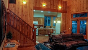 A wooden interior with a staircase, a dining area with a sofa, and a kitchen visible in the background.