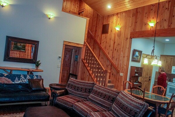 A cozy living room with a wooden staircase, a dining area, and a kitchen visible through an open door.