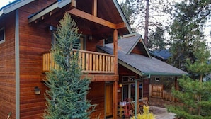 A two-story log cabin with a balcony, a covered porch, and a small deck area.