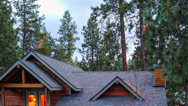 A log cabin with a balcony and a porch, surrounded by trees.