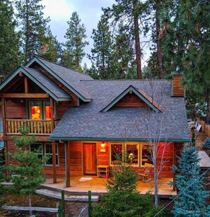A log cabin with a balcony and a porch, surrounded by trees.