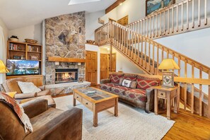 A cozy living room with a stone fireplace, wooden staircase, and comfortable seating.