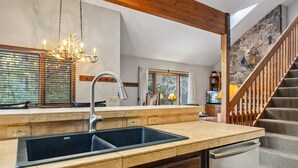 Een keuken met een dubbele spoelbak, houten kastjes, een kroonluchter en een stenen muur met een hert-muurdecoratie.
