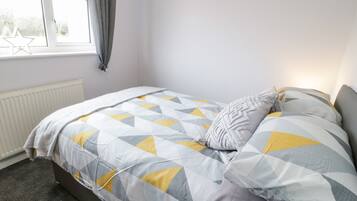 Un dormitorio con cama, ventana con cortinas, radiador y piso cubierto de alfombra.