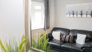 Un canapé en cuir noir agrémenté de plusieurs coussins, une fenêtre avec des rideaux et un tableau représentant des arbres accroché au mur.