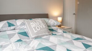 Un lit bien fait, avec une couvre-lit et des oreillers aux motifs géométriques, une lampe de chevet et une porte visible au fond.