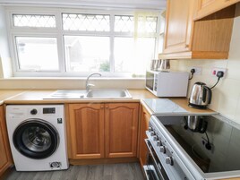 A compact kitchen with a washing machine, microwave, kettle, and oven.