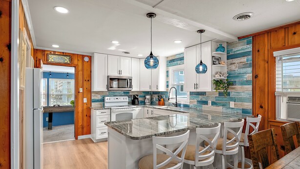 A modern kitchen with white cabinets, a central island with bar stools, and blue pendant lighting. - NEW LISTING! 15th St Beach Retreat #2 - 2 Bed/1 Bath Waterfront w/ Dock (Ocean City)