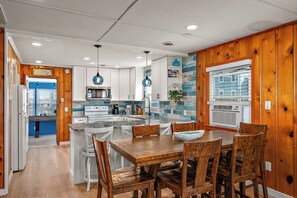Une cuisine moderne avec un lambris en bois, un îlot central, des armoires blanches et un coin repas avec des chaises en bois.