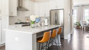 Une cuisine moderne avec des meubles blancs, un réfrigérateur en acier inoxydable et un îlot central doté de tabourets de bar.
