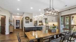 A spacious kitchen with white cabinets, a wooden dining table, and a hanging light fixture.
