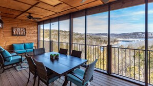 Une terrasse en bois avec une table et des chaises, un ventilateur de plafond et une vue sur une rivière et des arbres.
