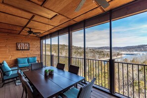 A wooden deck with a table and chairs, large windows with a view of a river and hills, and a ceiling fan. - 3BR+Loft Village At Indian Point 1406 near SDC -Free Tickets up to $500 Value (Branson)