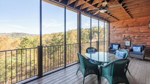 A wooden deck with a glass enclosure, wicker furniture, and a view of autumn foliage.