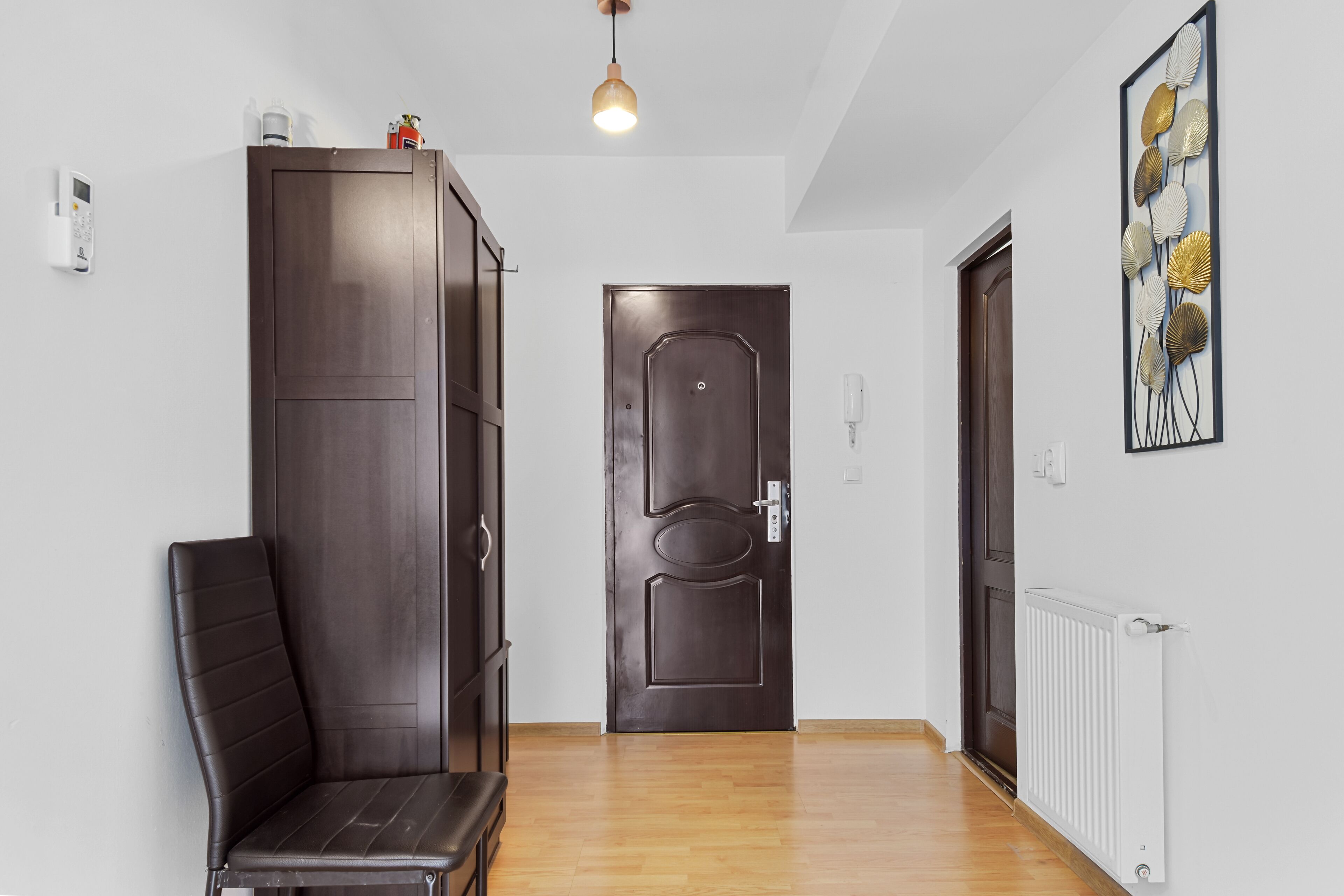 Un couloir avec une armoire en bois sombre, un banc, une porte et un radiateur.