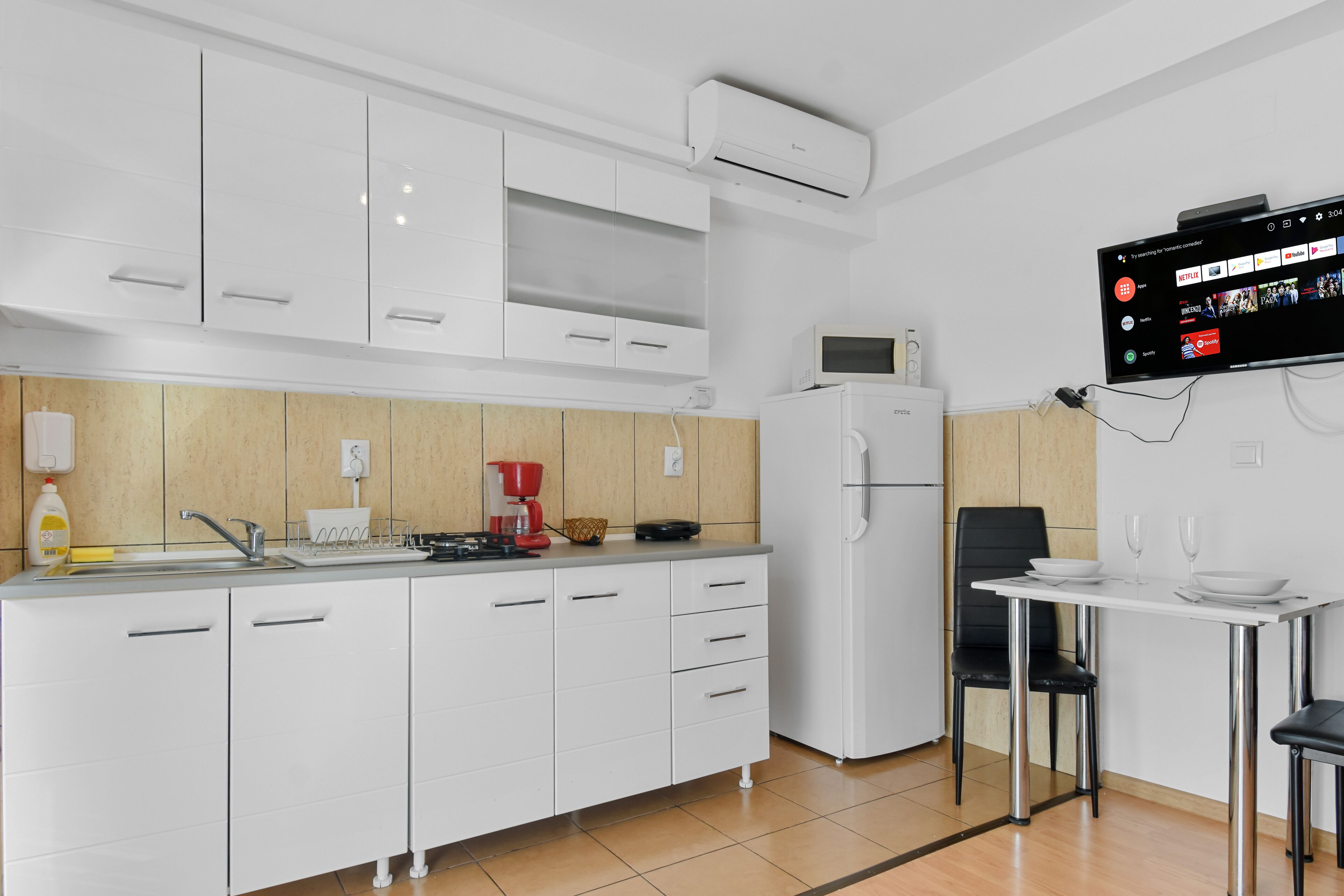 Una cocina moderna con armarios blancos, microondas, refrigerador, lavaplatos y una mesa de comedor con sillas.