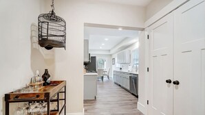 Un pasillo que conduce a una cocina con piso de madera, un lámpara colgante y una mesa con vasos y botellas.
