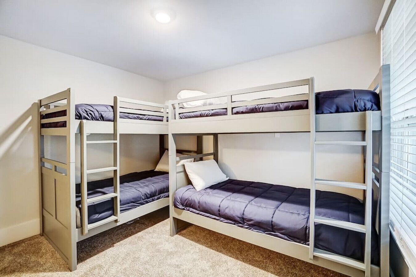 Un dormitorio con literas, una mesa pequeña y una ventana con persianas.