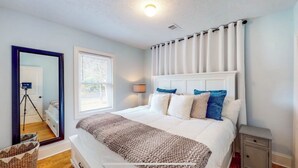 A bedroom with a bed, a nightstand, a lamp, a window with blinds, and a mirror. - Cheerful Four Bedroom home conveniently located (Augusta)