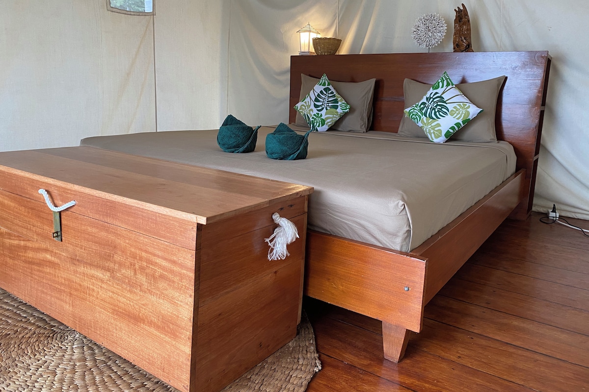 A bedroom with a wooden bed, a wooden chest of drawers, and a small table with a lamp.