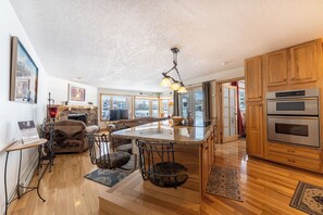 Una cocina amplia con gabinetes de madera, una isla grande con taburetes de bar, un horno empotrado y vistas a través de amplios ventanales.