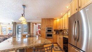 Una cocina moderna con encimeras de granito, electrodomésticos de acero inoxidable, armarios de madera y una isla grande con taburetes de bar.