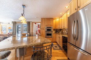 A modern kitchen with granite countertops, stainless steel appliances, wooden cabinets, and a large island with bar stools.