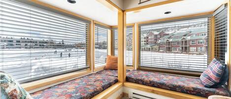 A corner room with a built-in bench and large windows with blinds, offering a view of a snowy street.