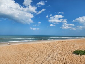 Ampia spiaggia sabbiosa con chiare tracce di pneumatici e alcune persone che camminano.