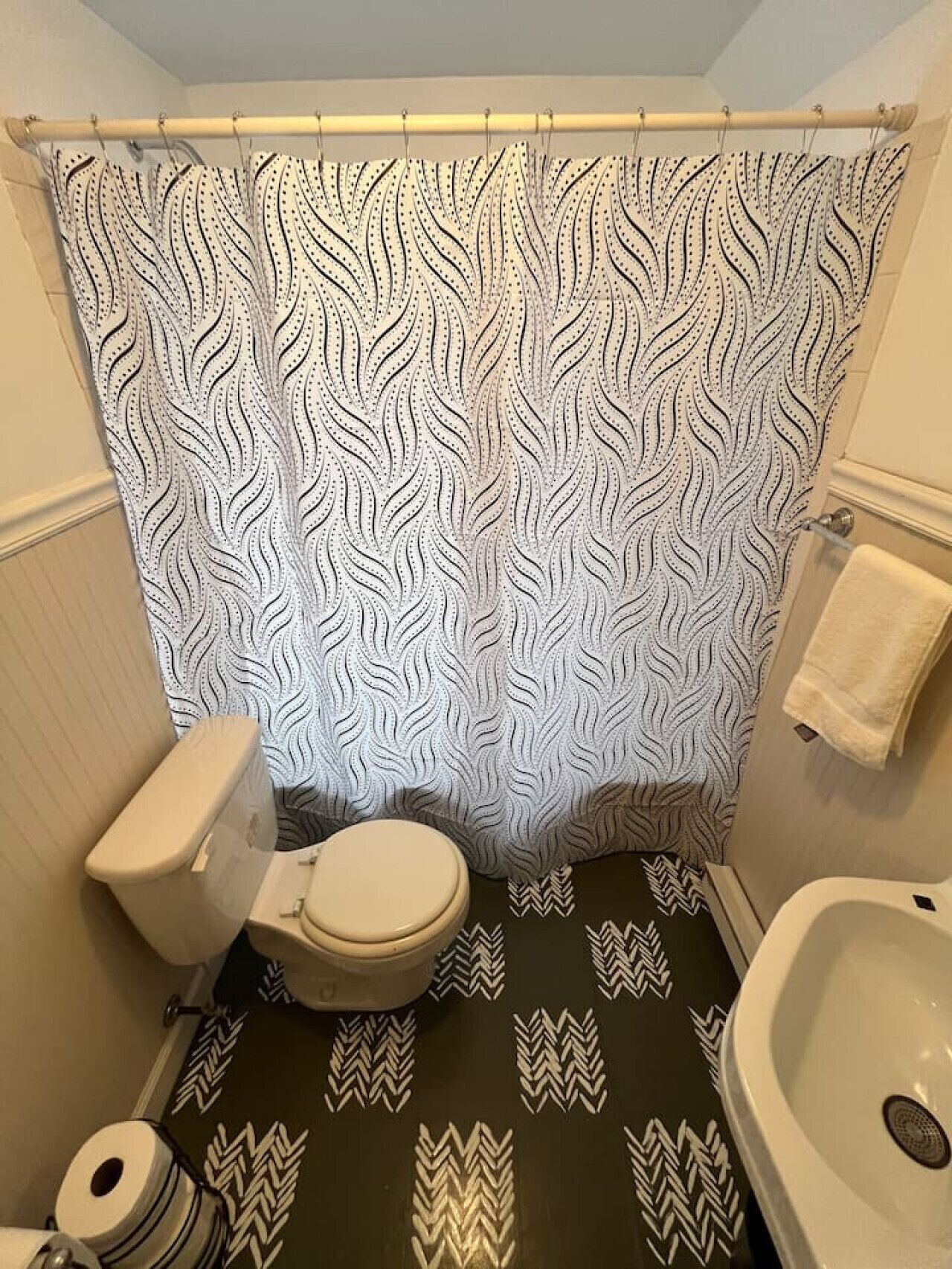 Un baño con cortina de ducha estampada, inodoro, lavamanos y suelo con diseño.