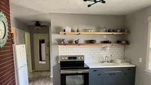 A compact kitchen with a built-in oven, a sink, and wooden shelves above. - Close to Downtown-Primary on Main-Fast Internet (Greensboro)