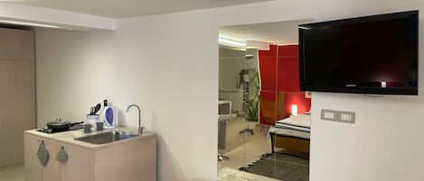 A compact living space with a kitchenette, a flat-screen TV, and a mirrored wall reflecting the room.