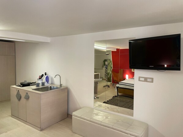 A compact living space with a kitchenette, a flat-screen TV, and a mirrored wall reflecting the room. - Maximum Loft's Nest (Palermo)