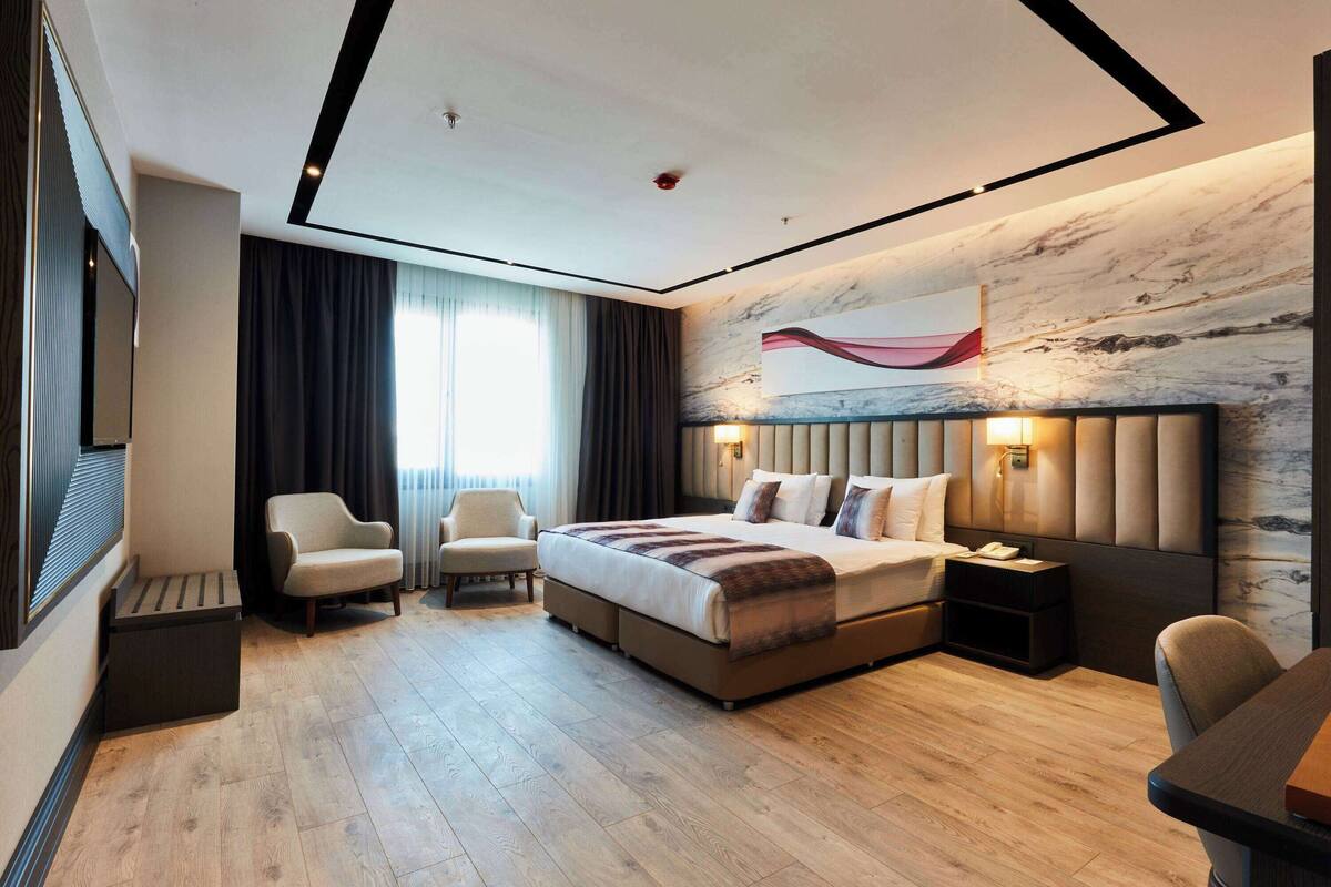 Una habitación de hotel moderna con una cama grande, un escritorio, dos sillones, un televisor y una pared de mármol.