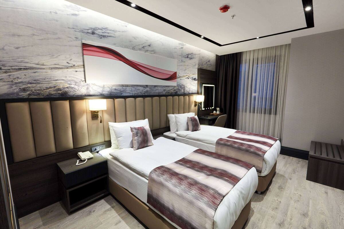 Habitación de hotel con dos camas, una pared de mármol, una obra de arte de gran tamaño, una mesita de noche con un teléfono y una ventana con cortinas.