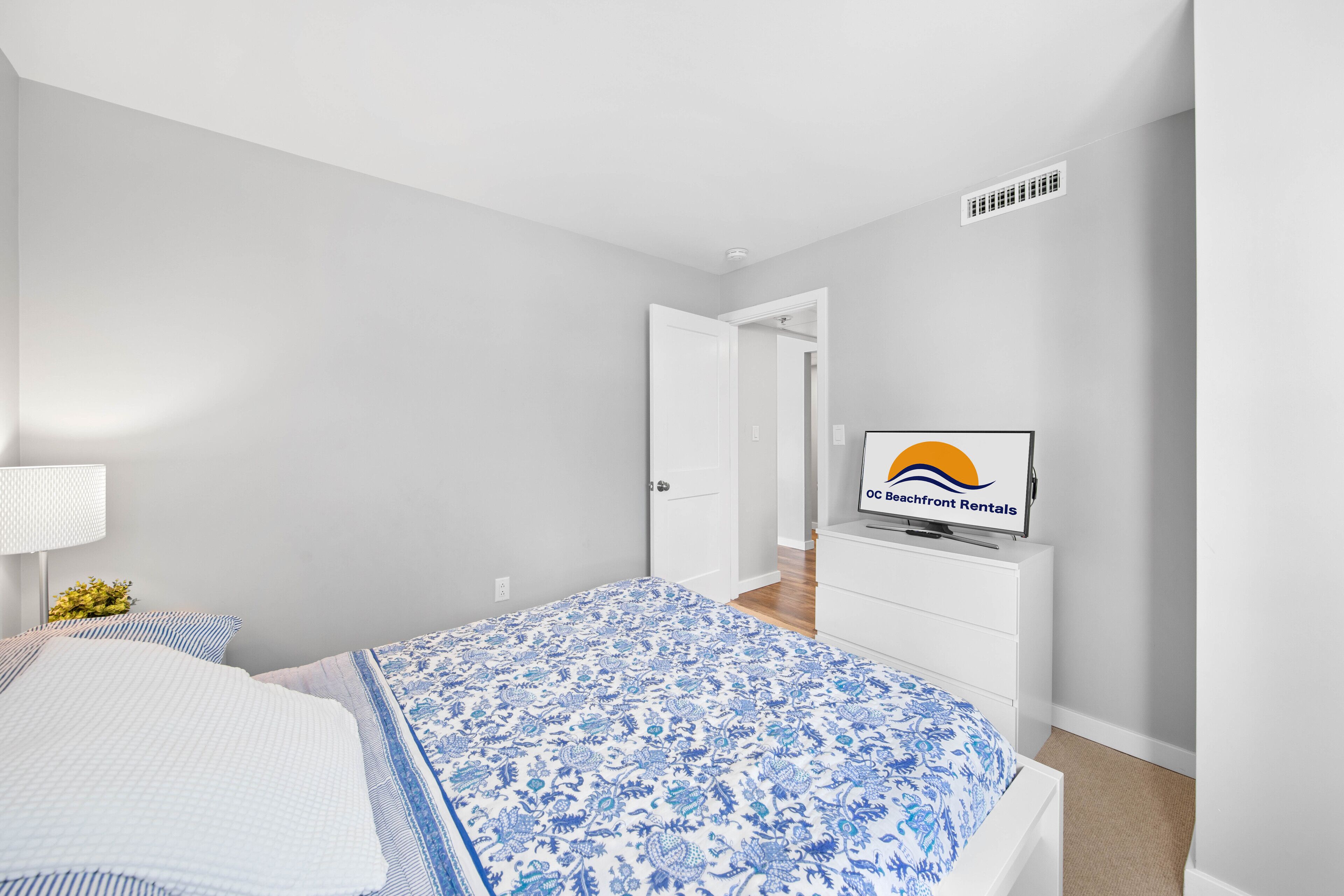 Une chambre à coucher avec un lit, un téléviseur posé sur une commode et une porte donnant sur une autre pièce.
