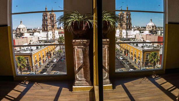 A room with a large window overlooking a cityscape, featuring a view of historic buildings and a clear sky.