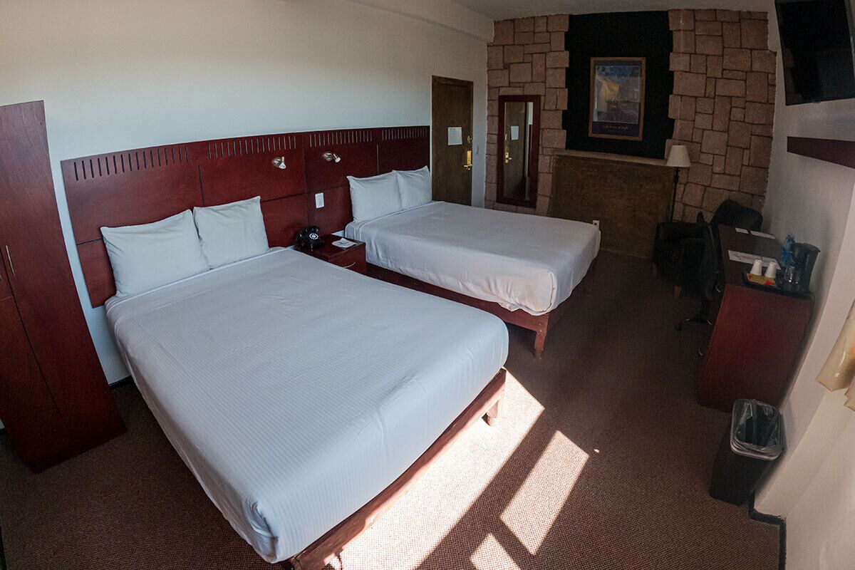Une chambre d’hôtel avec deux lits, une tête de lit en bois, un mur en briques, une télévision et un bureau avec une chaise.
